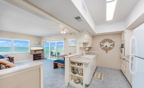 A modern kitchen with a central island, a dining area with a view of the ocean, and a living room with a TV.