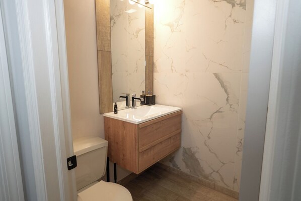 A bathroom with a white toilet, a wooden vanity with a white sink, and a marble-patterned wall.