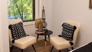 Deux chaises avec des coussins à motifs, une petite table ronde ornée d’une tête de cheval décorative et une fenêtre donnant sur des arbres.