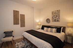 A bedroom with a bed, bedside tables, a chair, and wall art.