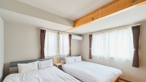 Habitación de hotel con dos camas, viga de techo de madera, unidad de aire acondicionado y cortinas en las ventanas.