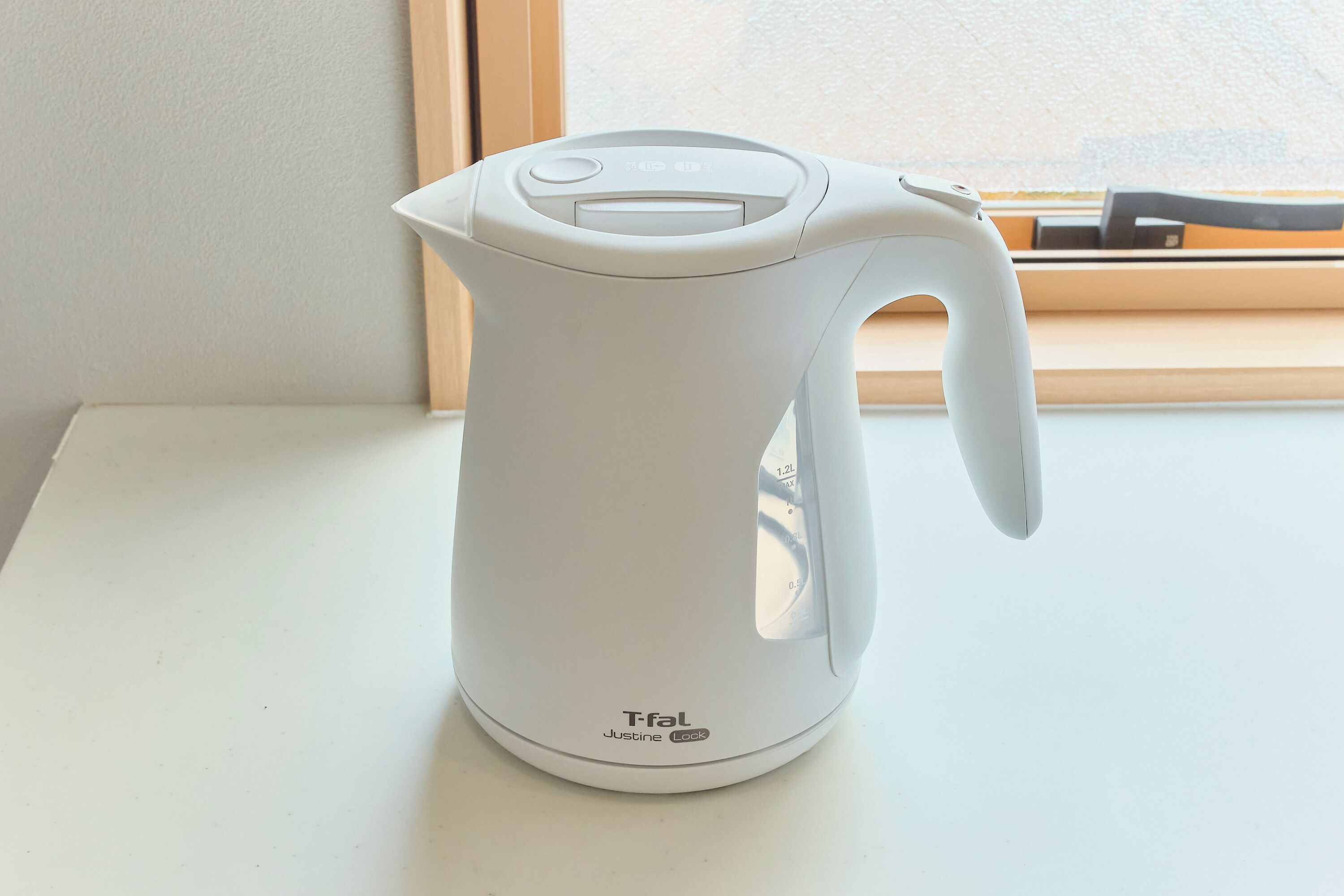A white electric kettle on a white surface near a window.