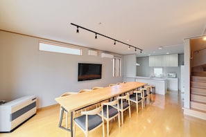 Una cuina moderna amb una illa central, una zona de menjador amb una taula llarga i cadires, i una escala que condueix a un nivell superior.