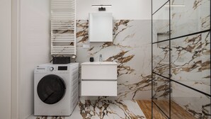 A modern bathroom with a washing machine, a sink, and a glass shower enclosure. - Business Park Classy Elegant Studio (Warszawa)