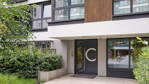 A modern building with a large glass entrance, a concrete planter with greenery, and a metal security camera. - Business Park Classy Elegant Studio (Warszawa)