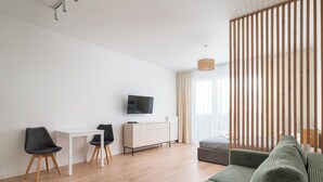 A modern living room with a sofa, a TV, a white table, and a wooden partition. - Business Park Classy Elegant Studio (Warszawa)