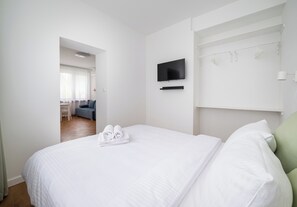 Ein Hotelzimmer mit Bett, Wandfernseher, kleinem Tisch und einer Sitzecke mit Sofa und Sesseln.
