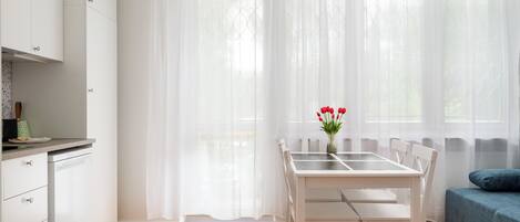 A modern kitchen with white cabinets, a dining table with chairs, and a blue sofa.
