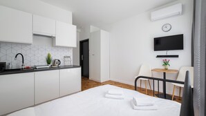 A modern hotel room with a kitchenette, a bed with towels, a TV, and a small table with chairs. - Metro Służew Apartment #2 (Warszawa)