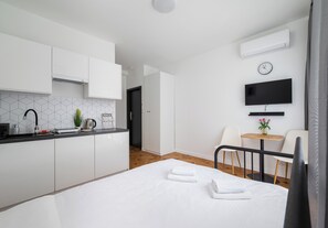A modern hotel room with a kitchenette, a bed with towels, a TV, and a small table with chairs. - Metro Służew Apartment #2 (Warszawa)