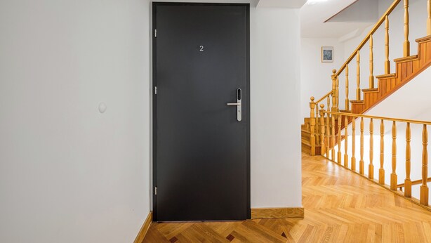 A black door with a number '2' on it, a wooden staircase with a railing, and a wooden floor. - Metro Służew Apartment #2 (Warszawa)
