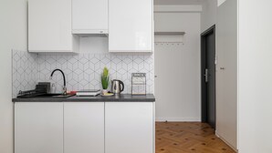 A modern kitchen with white cabinets, a black countertop, a geometric backsplash, and a wooden floor. - Metro Służew Apartment #2 (Warszawa)