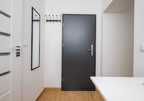 Quarto moderno com porta escura, cabide, parede branca e chão de madeira.