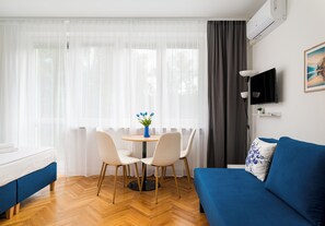 Ein Zimmer mit einem Bett, einem blauen Sofa, einem Esstisch mit Stühlen, einem Fernseher und einem Fenster mit Vorhängen.
