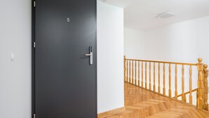 Eine schwarze Tür mit der Zahl 5, eine Holztreppe mit Geländer und ein Lichtschalter an der Wand.