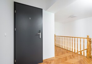 Una puerta negra con el número 5, una escalera de madera con barandilla y un interruptor de luz en la pared.