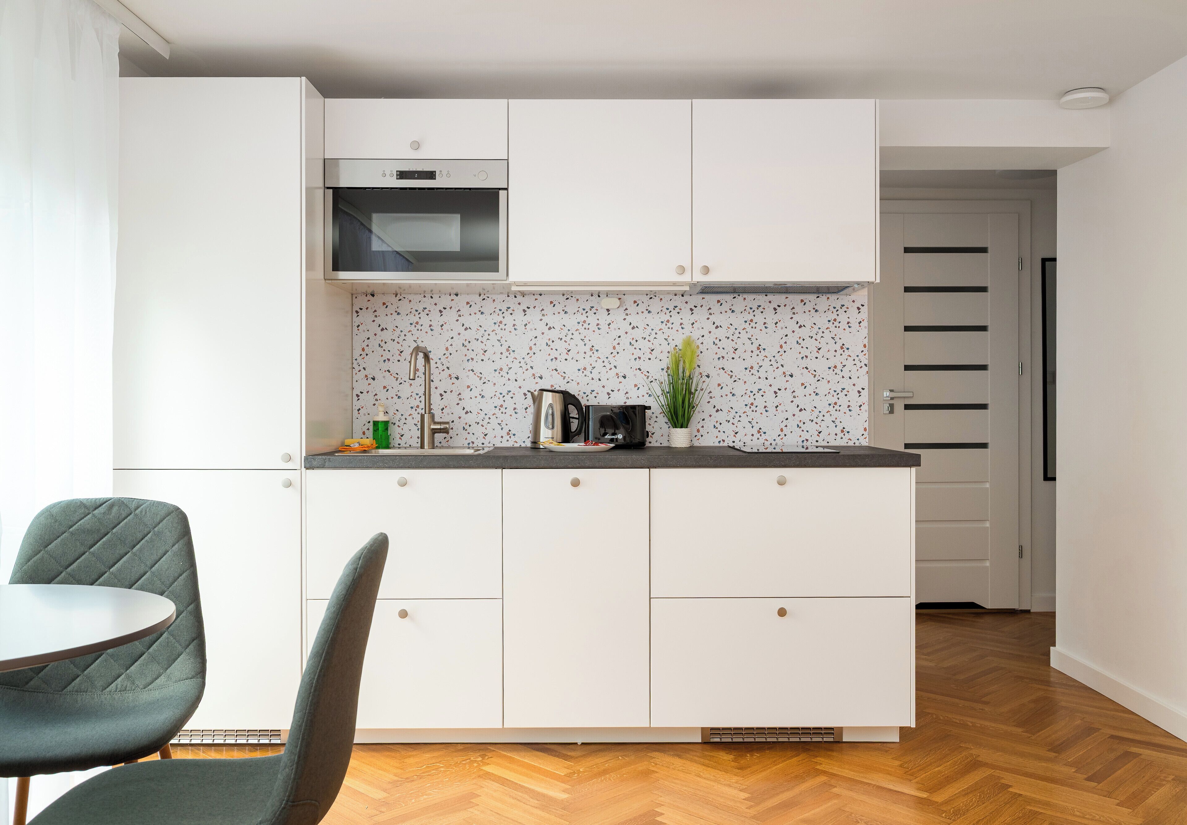 Une cuisine moderne avec des armoires blanches, un four encastré et un parquet en bois disposé en chevrons.