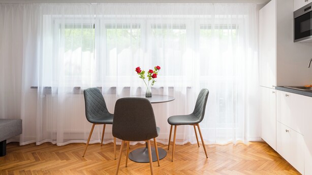 A modern kitchen with white cabinets, a round dining table, two chairs, and a vase with flowers. - Metro Służew Apartment #6 (Warszawa)