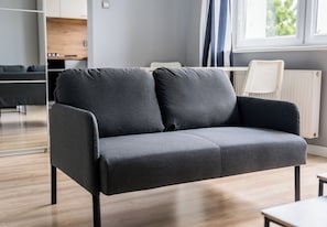 A modern living room with a grey sofa, wooden flooring, and a view of the kitchen and dining area. - Grunwald Comfort Apartment (Poznań)