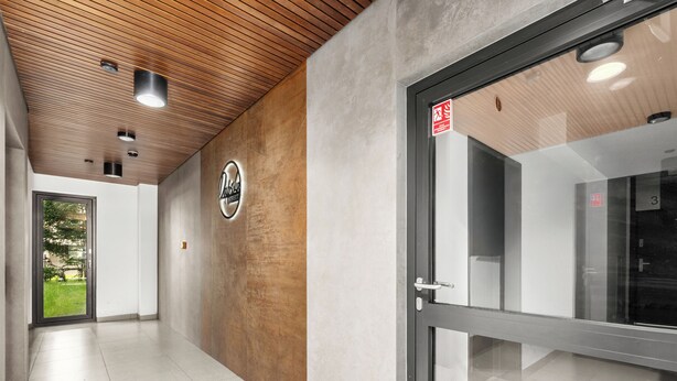 A hallway with a wooden ceiling, a glass door with a number, and a sign on the wall. - Tauron Arena Harmony Apartment (Kraków)