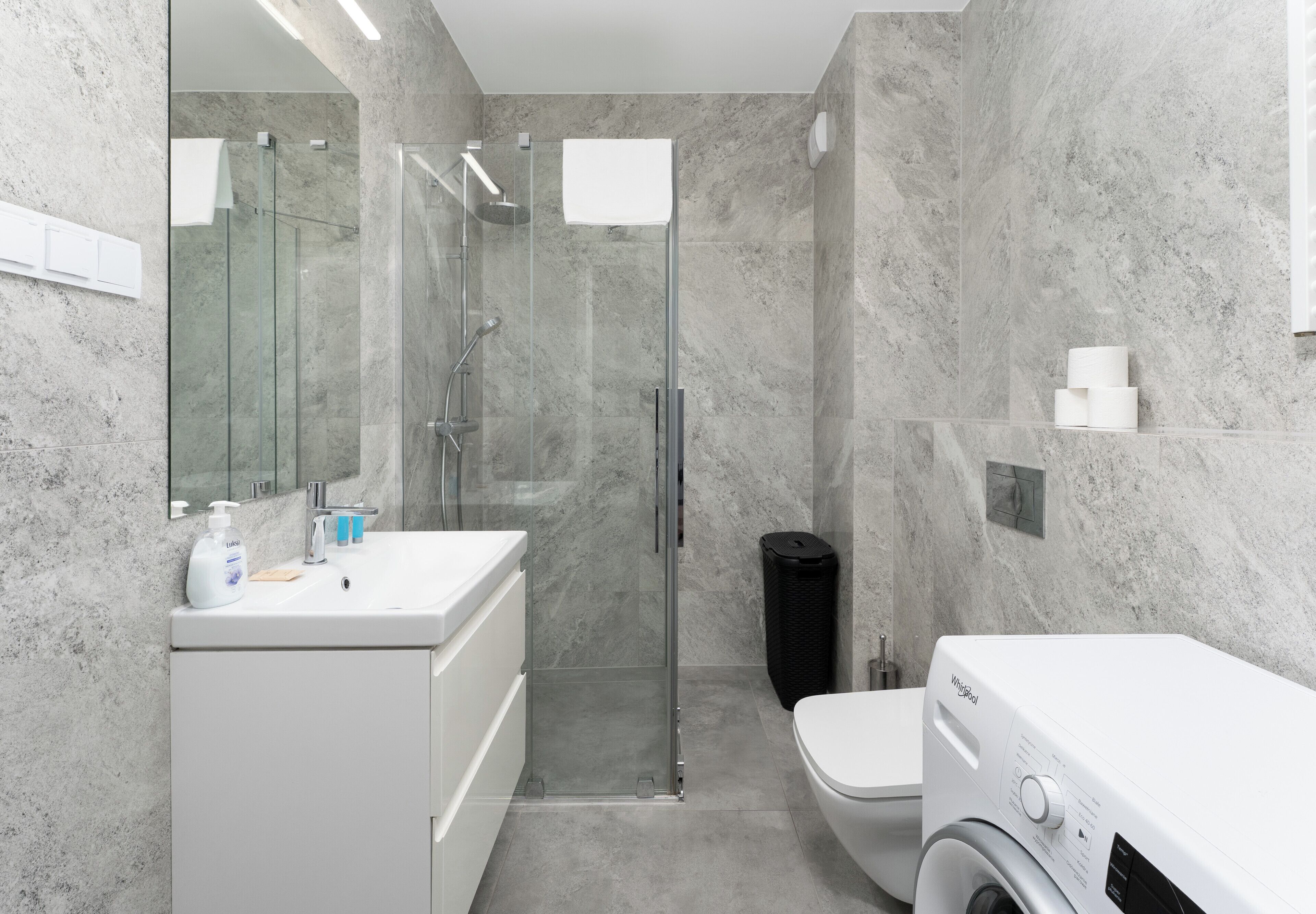 Une salle de bain moderne avec une douche à parois de verre, un lavabo blanc, des toilettes et un lave-linge.