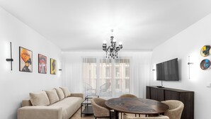 Una sala de estar moderna con un sofá, mesa de comedor, sillas, candelabro, obras de arte y televisor.