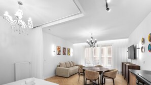 Una habitación de hotel moderna con una cama, un área de comedor con una mesa y sillas, un sofá, un televisor y obras de arte en las paredes.