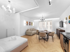 A modern hotel room with a bed, a dining area with a table and chairs, a sofa, a TV, and artwork on the walls. - Kraków Główny Superior Studio (Kraków)