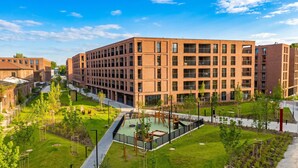 Un edificio moderno de varios pisos con fachada de ladrillo, rodeado de zonas verdes cuidadas y senderos.