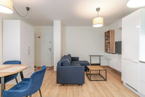 A modern living room with a sofa, a dining table with chairs, a TV mounted on the wall, and a wooden cabinet. - Chopina Stylish Apartment (Katowice)