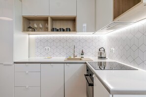 Moderni keittiö, jossa on valkoiset kaapit, ruostumattomasta teräksestä valmistettu allas ja geometrisesti kuvioitu välitila.