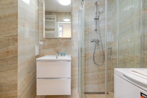 A modern bathroom with a glass-enclosed shower, a white sink with a mirror above, and a white cabinet below. - Chopina Stylish Apartment (Katowice)