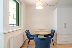 A room with a round table, two blue chairs, a white cabinet, and a window with a view of a building. - Chopina Stylish Apartment (Katowice)