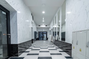 A hallway with white marble walls and a black and white checkered floor, leading to a door with a glass panel. - Chopina Stylish Apartment (Katowice)