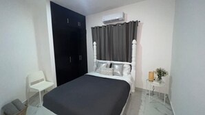 A bedroom with a bed, a wardrobe, an air conditioning unit, a chair, and a small table with a vase. - Beautiful apartment in the city center (Santo Domingo)