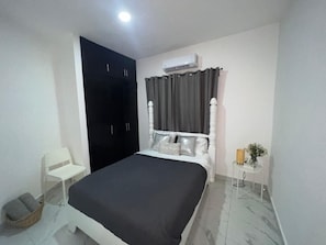 A bedroom with a bed, a wardrobe, an air conditioning unit, a chair, and a small table with a vase. - Beautiful apartment in the city center (Santo Domingo)