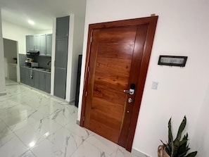 A wooden door with a metal handle, a kitchen area with grey cabinets, and a sign on the wall. - Beautiful apartment in the city center (Santo Domingo)