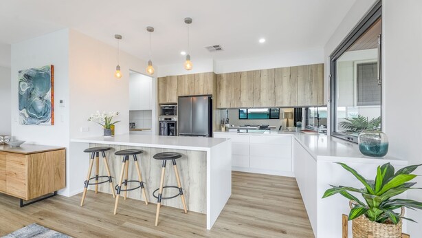 Een moderne keuken met een centraal eiland, barkrukken, houten kastjes en hanglampen.
