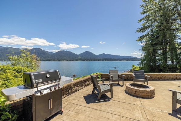 An outdoor patio with a grill, seating, and a view of a lake and mountains.