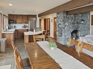 A modern kitchen with wooden cabinets, a stone fireplace, and a dining area with a long wooden table and chairs.