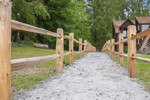 A gravel path bordered by wooden fences, leading to a building with a sloped roof.