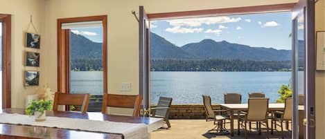 A dining area with a view of a lake and mountains, wooden furniture, and a large window.