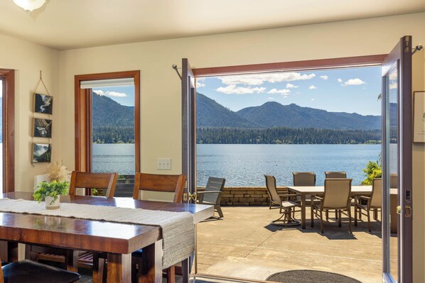A dining area with a view of a lake and mountains, wooden furniture, and a large window.