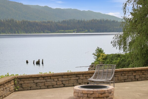 A lakeside view with a stone bench and a fire pit.