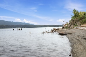 A calm lake with a rocky shoreline, distant mountains, and clear skies.