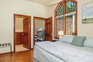 A bedroom with a bed, a window with a view, a door, and a shelf with books.