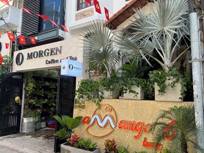 Un edificio con un letrero que dice 'MORGEN Coffee and Tea', rodeado de plantas en macetas y un muro decorativo con diseño de olas.
