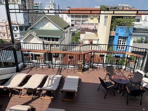 Terraza en la azotea con sillones, una mesa de madera y sillas, rodeado por una barandilla de metal negro.
