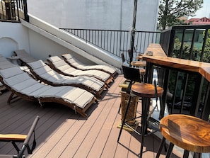 Terraza con tumbonas, una mesita y una zona de bar con taburetes.