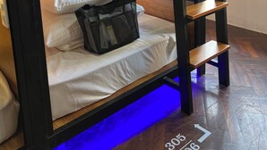 A bunk bed with a headboard, a bedside table, a bag, and a window with curtains. - Amango Village (Ho Chi Minh City)